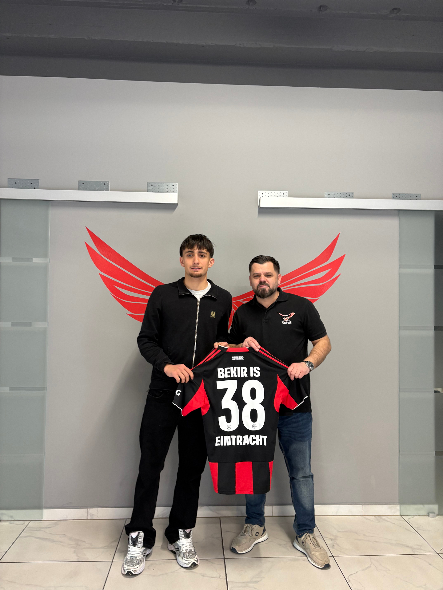 Besir Memishi mit personalisiertem Eintracht-Trikot „BEKIR IS 38" vor dem Adler-Cut-Logo im Salon